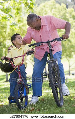 Stock Photograph - Grandfather and grandson on bikes outdoors smiling. Fotosearch