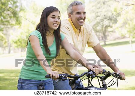 Stock Image - Man and girl on bikes outdoors smiling. Fotosearch