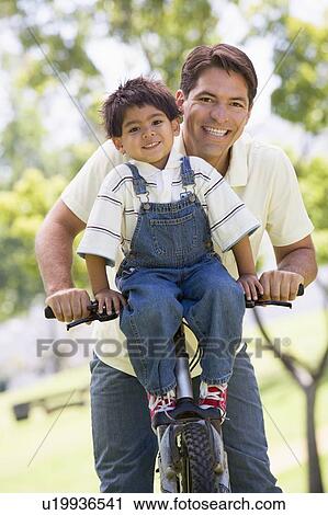 Stock Image - Man and young boy on a bike outdoors smiling. Fotosearch