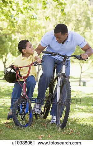 Stock Image - Man and young boy on bikes outdoors smiling. Fotosearch