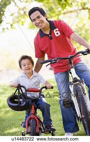 Stock Image - Man and young boy on bikes outdoors smiling. Fotosearch