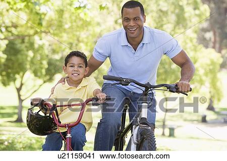 Stock Image - Man and young boy on bikes outdoors smiling. Fotosearch