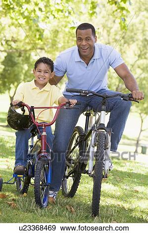 Stock Photo - Man and young boy on bikes outdoors smiling. Fotosearch