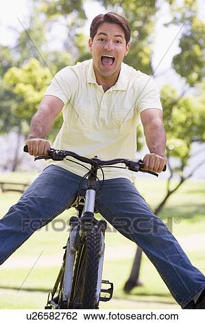 Stock Image - Man outdoors on bike with legs out. Fotosearch