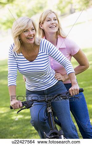 Two friends on one bike outdoors smiling View Large Photo Image Picture - Two friends on one bike outdoors smiling. Fotosearch