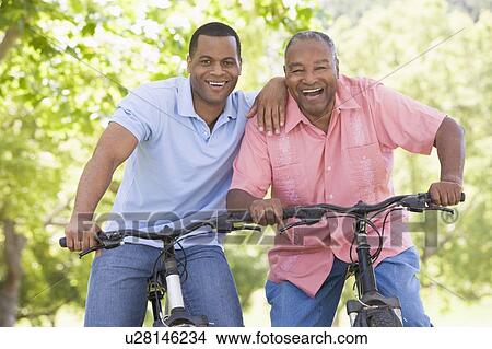 Picture - Two men on bikes outdoors smiling. Fotosearch