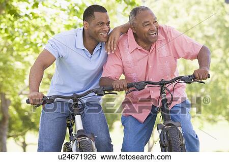 Stock Photograph - Two men on bikes outdoors smiling. Fotosearch