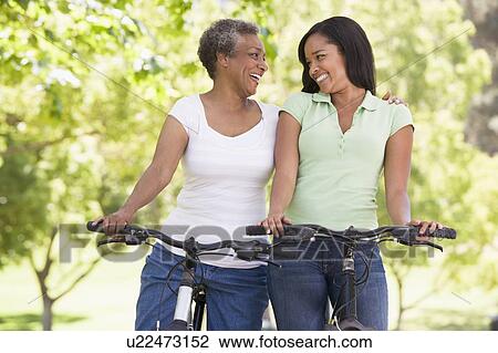 Stock Image - Two women on bikes outdoors smiling. Fotosearch