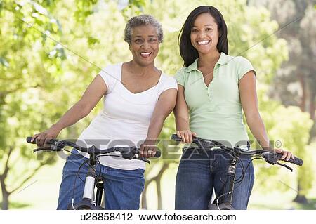 Stock Image - Two women on bikes outdoors smiling. Fotosearch