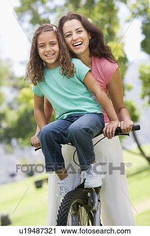 Stock Image - Woman and young girl on a bike outdoors smiling. Fotosearch