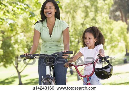 Stock Photograph - Woman and young girl on bikes outdoors smiling. Fotosearch