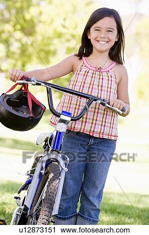 Stock Image - Young girl with bicycle outdoors smiling. Fotosearch