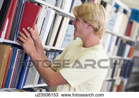 Stock Image - Man in library pulling book off a shelf (depth of field). Fotosearch