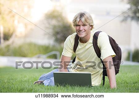 Picture - Man outdoors sitting on grass with laptop (selective focus). Fotosearch
