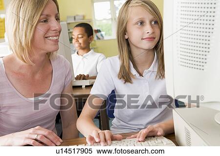 Stock Photography - Student and teacher at computer terminal typing with student in background (selective focus). Fotosearch