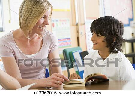 Stock Photograph - Student in class reading book with teacher. Fotosearch