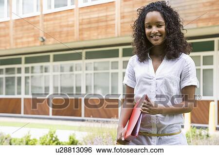 Stock Photograph - Student standing outdoors smiling and holding binder. Fotosearch