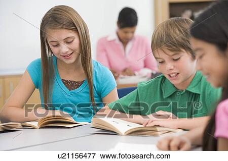 Stock Photo - Students in class reading with teacher in background (selective focus). Fotosearch