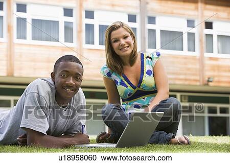 Stock Image - Two students outdoors on lawn with laptop. Fotosearch