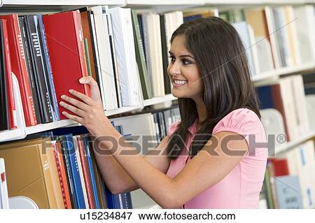 Stock Photo - Woman in library pulling book off a shelf (depth of field). Fotosearch