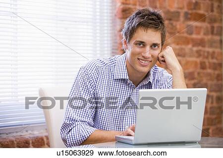 Stock Photo - Businessman sitting in office with laptop smiling. Fotosearch