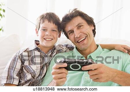 Stock Photo - Man and young boy with handheld game smiling. Fotosearch