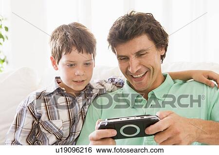 Man and young boy with handheld game smiling View Large Photo Image Stock Photograph - Man and young boy with handheld game smiling. Fotosearch