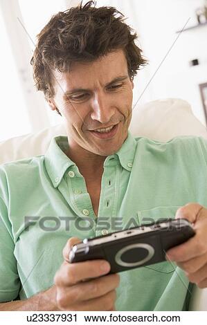 Man in living room playing handheld videogame smiling View Large Photo Image Stock Image - Man in living room playing handheld videogame smiling. Fotosearch