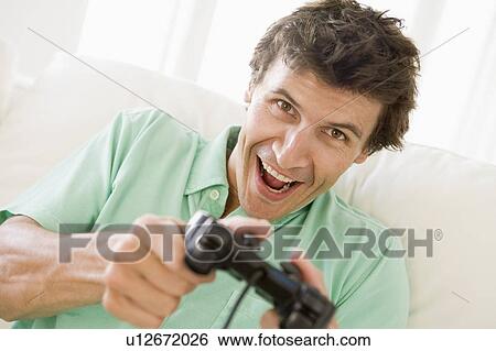 Stock Photograph - Man in living room playing videogames smiling. Fotosearch