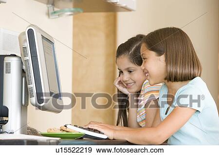 Stock Photo - Two young girls in kitchen with computer smiling. Fotosearch