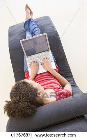 Stock Image - Woman sitting in chair using laptop. Fotosearch