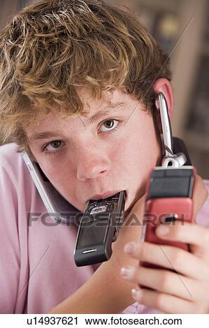 Stock Image - Young boy in bedroom holding many cellular phones. Fotosearch
