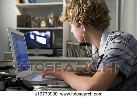 Young boy in bedroom using laptop and listening to MP3 player View Large Photo Image Stock Photo - Young boy in bedroom using laptop and listening to MP3 player. Fotosearch