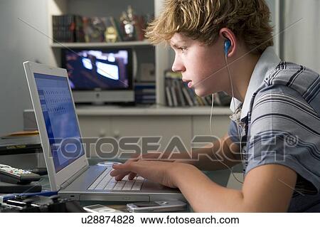 Stock Photo - Young boy in bedroom using laptop and listening to MP3 player. Fotosearch