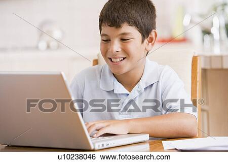 Stock Photograph - Young boy in kitchen with laptop and paperwork smiling. Fotosearch