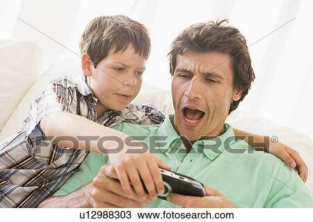 Stock Image - Young boy taking handheld game from unhappy man. Fotosearch