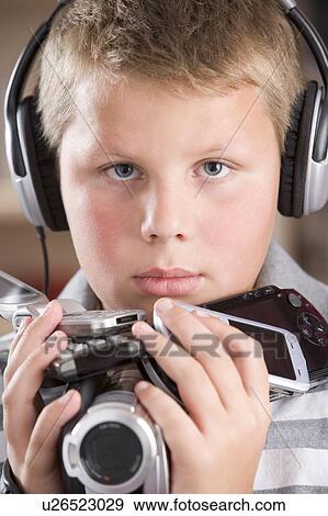 Young boy wearing headphones in bedroom holding many electronic devices View Large Photo Image Stock Photo - Young boy wearing headphones in bedroom holding many electronic devices. Fotosearch