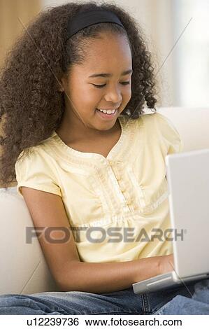 Stock Photograph - Young girl in living room using laptop and smiling. Fotosearch