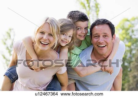 Picture - Couple giving two young children piggyback rides smiling. Fotosearch