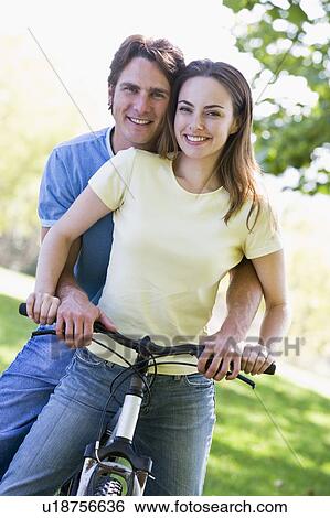 Couple on a bike outdoors smiling View Large Photo Image Stock Photograph - Couple on a bike outdoors smiling. Fotosearch