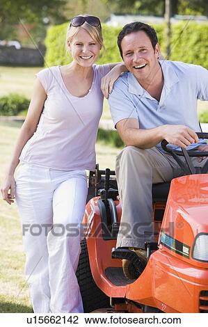 Stock Image - Couple outdoors with lawnmower smiling. Fotosearch