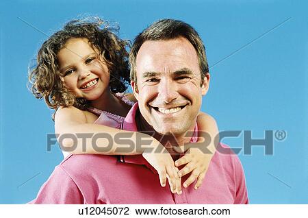 Stock Image - Father giving daughter piggyback ride outdoors smiling. Fotosearch