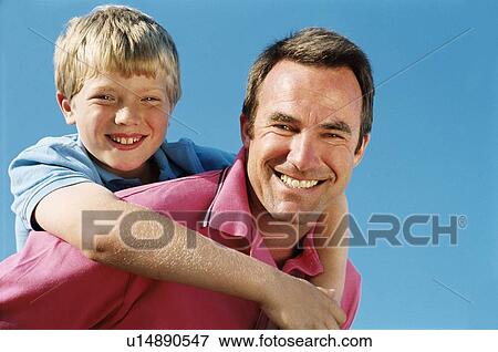 Stock Photo - Father giving son piggyback ride outdoors smiling. Fotosearch