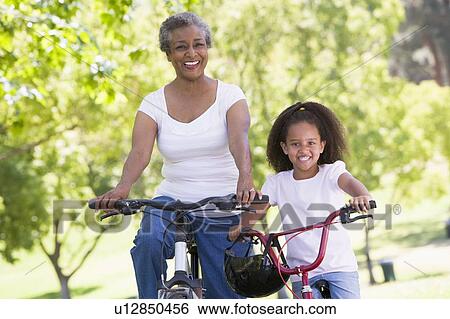 Stock Photograph - Grandmother and granddaughter on bikes outdoors smiling. Fotosearch