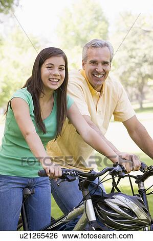 Stock Photograph - Man and girl on bikes outdoors smiling. Fotosearch