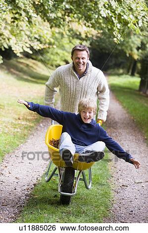 Man and young boy walking on path outdoors with wheelbarrow smiling (selective focus) View Large Photo Image Stock Photograph - Man and young boy walking on path outdoors with wheelbarrow smiling (selective focus). Fotosearch