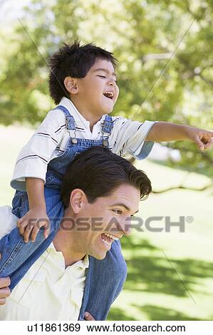 Man giving young boy shoulder ride outdoors smiling View Large Photo Image Stock Photo - Man giving young boy shoulder ride outdoors smiling. Fotosearch