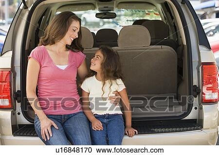 Stock Image - Woman with young girl sitting in back of van smiling. Fotosearch
