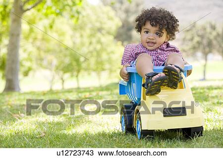 Young boy outdoors playing on toy dump truck smiling View Large Photo Image Stock Image - Young boy outdoors playing on toy dump truck smiling. Fotosearch