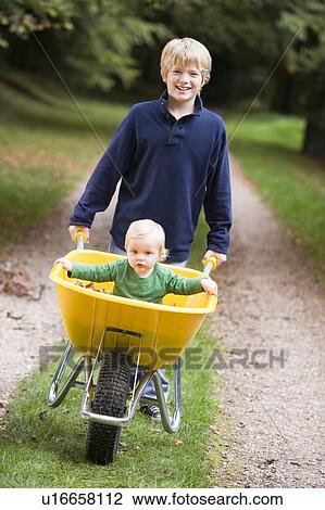 Young boy outdoors pushing baby brother in wheelbarrow and smiling (selective focus) View Large Photo Image Stock Image - Young boy outdoors pushing baby brother in wheelbarrow and smiling (selective focus). Fotosearch